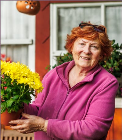 Elderly woman smiling with potted flowers.