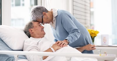 A caregiver lovingly comforts a resident in bed.