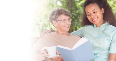 Senior resident reading with staff member outdoors