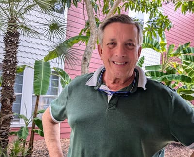 Smiling man in outdoor space surrounded by greenery.