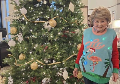 Resident in festive sweater by a decorated Christmas tree.
