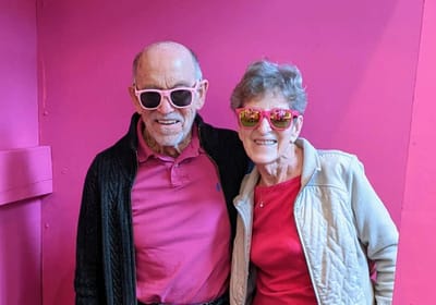 Two smiling seniors wearing colorful sunglasses.