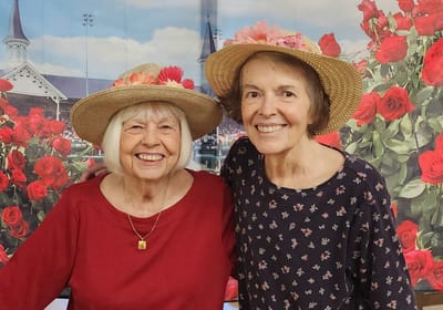 Two smiling women wearing straw hats among flowers.