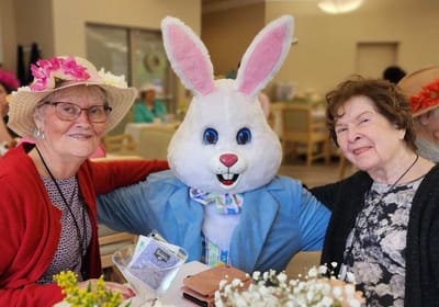 Two residents with a costumed bunny in a common area.