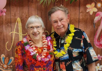 Elderly couple celebrating with leis and smiles.