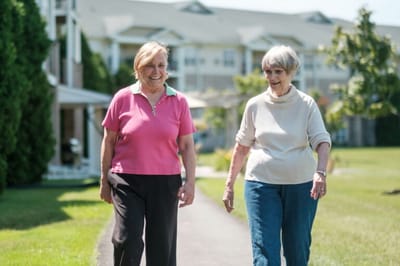 Two residents walking on a pathway outside the facility
