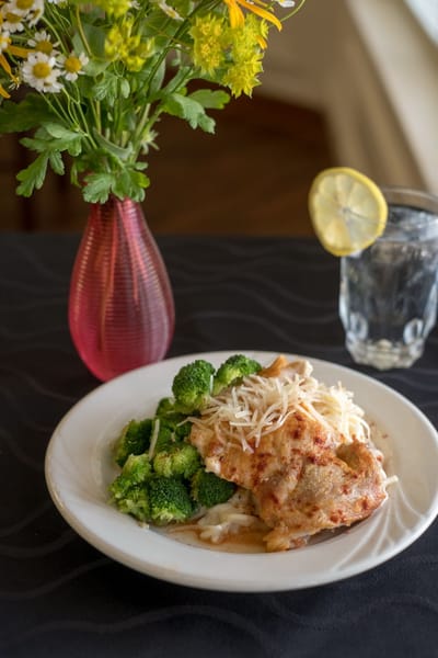 Plate of chicken with broccoli and a vase of flowers