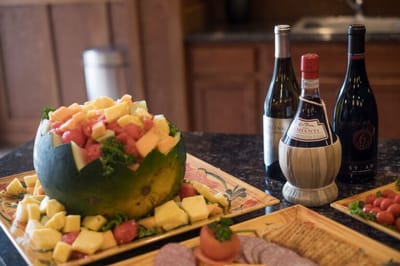 A fruit and cheese platter with wine bottles in the background