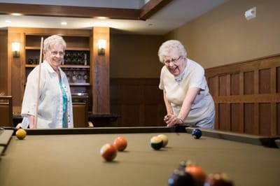 Two residents playing billiards in an indoor game area