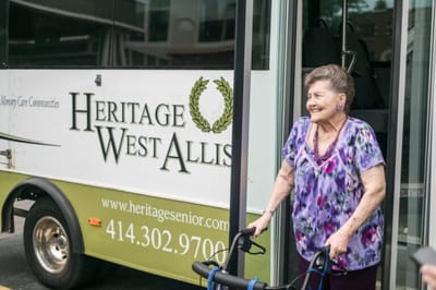 A resident smiling while using a walker near a bus.