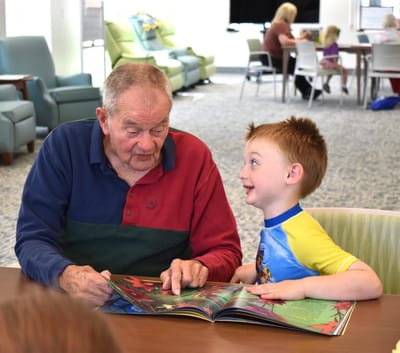 An elderly man and a child reading together in a common area