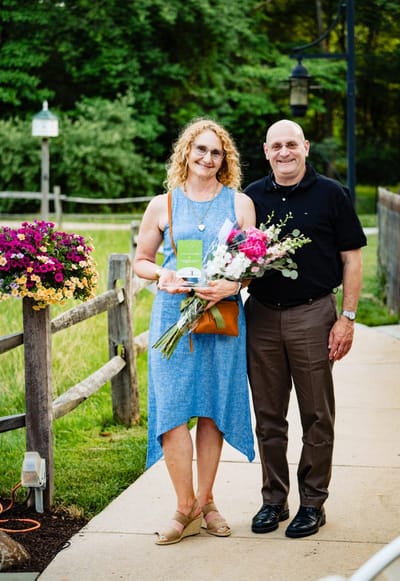 Two smiling individuals in an outdoor setting with flowers
