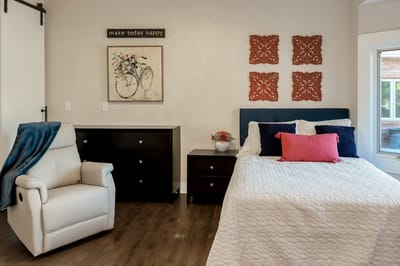 A well-decorated resident room with a bed and chair