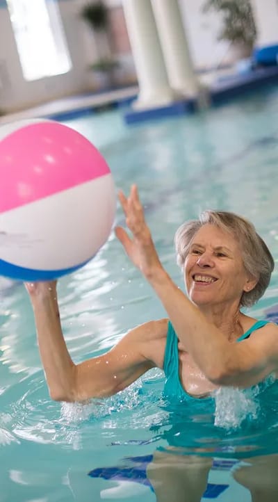 An elderly woman playing with a beach ball in a swimming pool