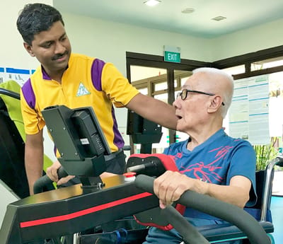 Staff assisting an elderly resident with exercise equipment