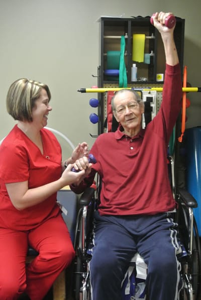 Therapist assisting a resident with weights in an activity room