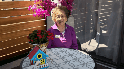 A resident enjoying the outdoors with flowers and a decorative house