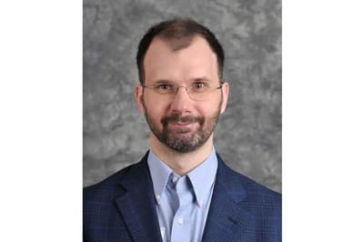 A professional headshot of a man wearing glasses