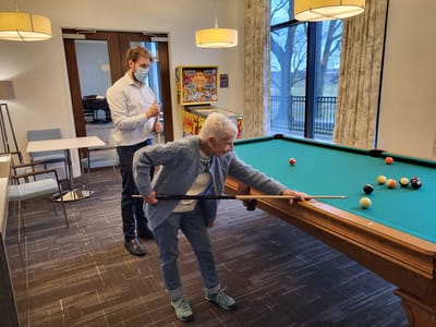 Senior resident playing billiards with staff assistance