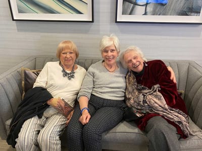 Three senior women smiling on a couch in a common area