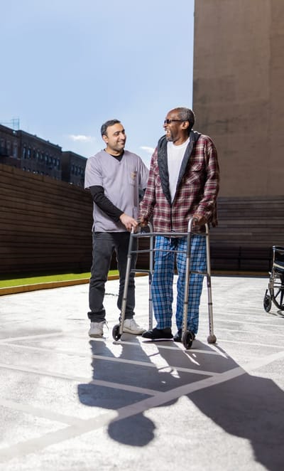 Staff assisting a resident outdoors with a walker