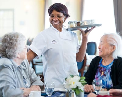 A staff member serving food to residents in a dining area