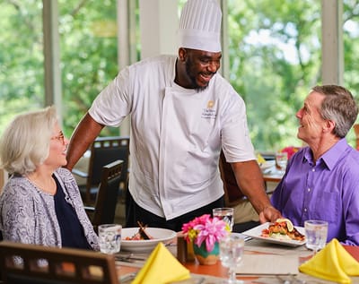 Chef serving a meal to two residents in the dining room
