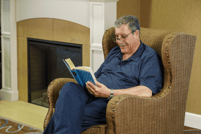 A resident reading a book in a cozy chair by the fireplace
