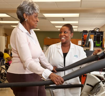 A resident using a treadmill with assistance from staff