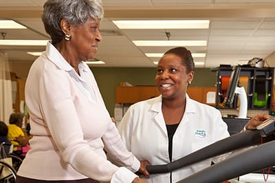 A resident using a treadmill with assistance from staff