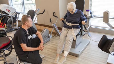 A staff member assisting a resident with rehabilitation equipment