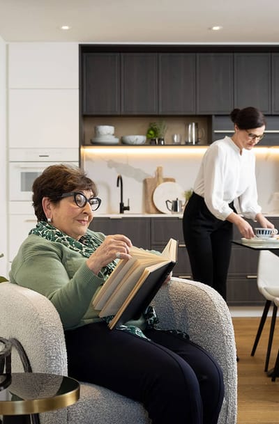 A resident enjoying a book with staff in a cozy living space
