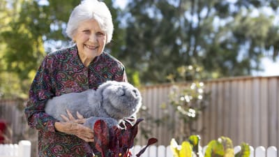 A resident smiling while holding a plush animal in a garden