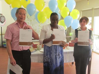 Three staff members holding achievement certificates at a celebration