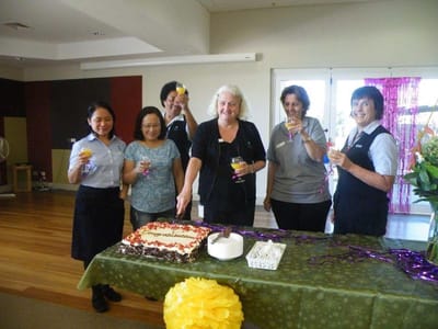 Celebration with staff and residents holding drinks and a cake