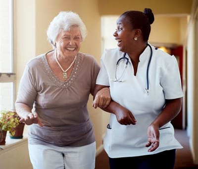 A caregiver assisting a smiling resident in a hallway