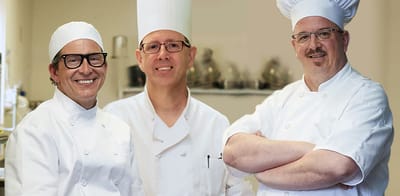 Three chefs smiling in a kitchen.