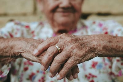 Elderly woman's hands with a ring resting on her lap.