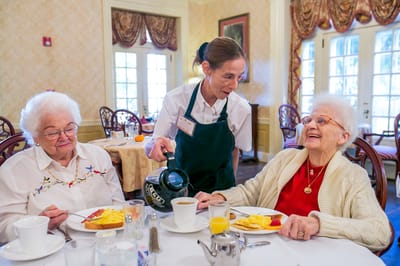Two elderly women enjoying breakfast with a staff member.