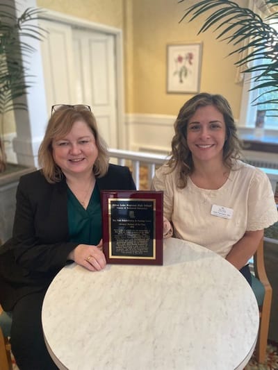 Two women holding an award in a common area