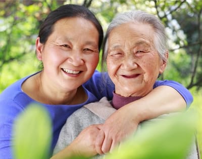 A senior woman and her caregiver smiling together outdoors.
