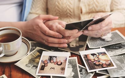 Elderly hands hold photos with tea nearby.