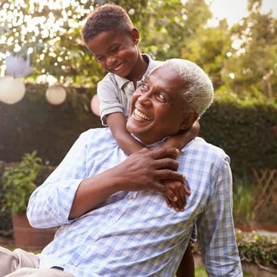 Elderly man playing with a young boy in a garden.