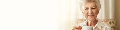 Elderly woman smiling while holding a cup.