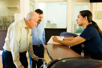 Staff assisting elderly resident at the reception desk.
