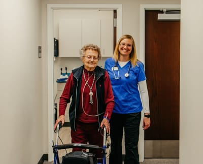 Elderly resident and staff member in a hallway.