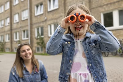 Child using binoculars outdoors with an adult.
