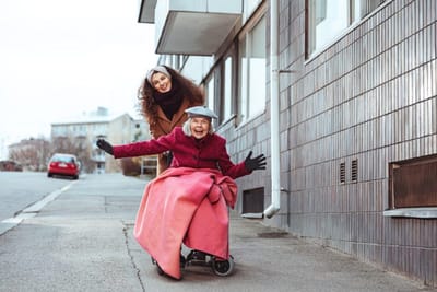 Senior woman in a wheelchair with a caregiver outdoors.