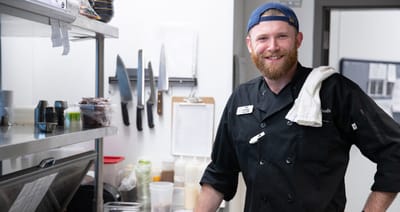 Chef smiling in kitchen with utensils around