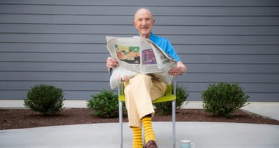Smiling resident reading a newspaper in the garden.